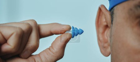 Photo for A swimmer man, wearing a blue swimming cap, is about to put an earplug, in a swimming pool, in a panoramic format to use as web banner or header - Royalty Free Image