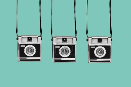 Photo for Three gray and black retro film cameras, hanging from their straps, on a blue background - Royalty Free Image