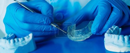 un dentista está ajustando una férula oclusal, utilizando una herramienta de metal, en un formato panorámico para usar como banner web o encabezado
