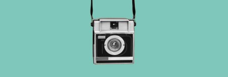 Téléchargez les photos : Une caméra de film rétro grise et noire suspendue à ses sangles sur un fond bleu, dans un format panoramique à utiliser comme bannière web ou en-tête - en image libre de droit