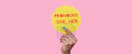Photo for A person holds a yellow round sign with the text my pronouns are she, her on a pink background, in a panoramic format to use as web banner or header - Royalty Free Image