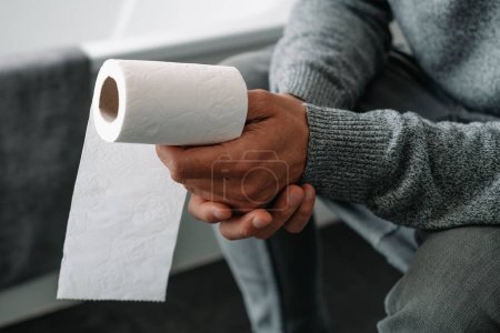 Téléchargez les photos : Gros plan d'un homme caucasien, assis dans les toilettes, ayant un rouleau de papier toilette dans sa main - en image libre de droit
