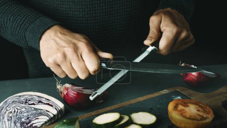Photo for A man steeling a kitchen knife with a honing steel at a table, in a panoramic format to use as web banner or header - Royalty Free Image