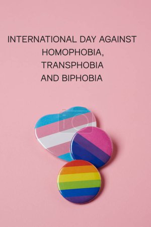 Téléchargez les photos : Le texte Journée internationale contre l'homophobie, la transphobie et la biphobie, et quelques insignes avec un drapeau de la fierté gay, un drapeau de la fierté transgenre et un drapeau de la fierté bisexuelle sur fond rose - en image libre de droit