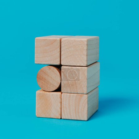 ein zylindrischer Spielzeugblock in einem Stapel rechteckiger Spielzeugblöcke, auf blauem Hintergrund, im quadratischen Format