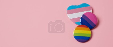 Foto de Algunas insignias estampadas con la bandera del arco iris, la bandera del orgullo transgénero y la bandera del orgullo bisexual, sobre un fondo rosa, en un formato panorámico para usar como banner web - Imagen libre de derechos