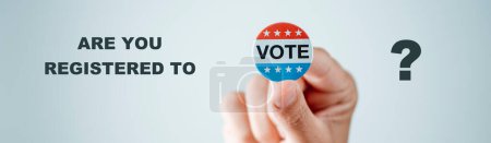 Foto de Un hombre tiene una insignia de voto para las elecciones de los Estados Unidos en su mano, en un fondo blanco, y la pregunta es si está registrado para votar, en un formato panorámico para usar como banner web - Imagen libre de derechos