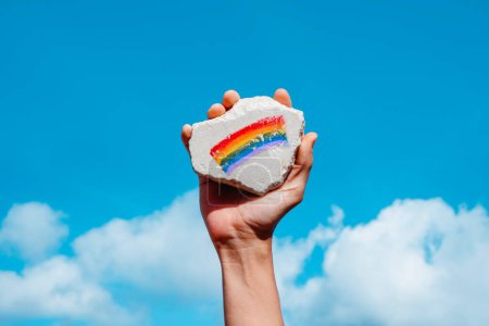 Photo for Man holding a rock with a rainbow flag in his hand, against the sky - Royalty Free Image