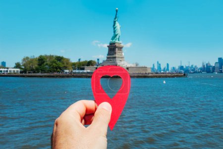 Téléchargez les photos : Un homme tient un marqueur rouge avec un cœur pointant la Statue de la Liberté, à Liberty Island, États-Unis, depuis la baie un jour de printemps ensoleillé - en image libre de droit