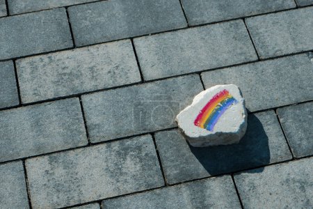 Téléchargez les photos : Gros plan d'un rocher plat avec un drapeau arc-en-ciel peint dessus, sur le trottoir d'une rue - en image libre de droit