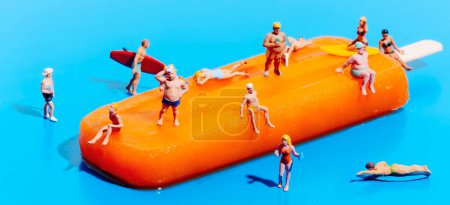 Photo for Closeup of some miniature people wearing swimsuit on an orange popsicle, on a blue background, in a panoramic format to use as web banner or header - Royalty Free Image