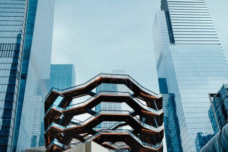 Photo for New York City, US - May 19, 2023: The famous Vessel structure, surrounded by several skyscrapers, at the public plaza of Hudson Yards, in New York City, United States - Royalty Free Image