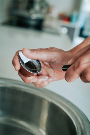 Foto de Un hombre caucásico utiliza un cuchillo para vaciar el café molido usado de una cápsula para arrojarlo al cubo de basura reciclable - Imagen libre de derechos