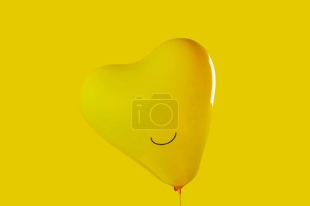 Photo for Closeup of an inflated yellow heart-shaped balloon with a smile drawn in it on a yellow background, to depict happiness - Royalty Free Image