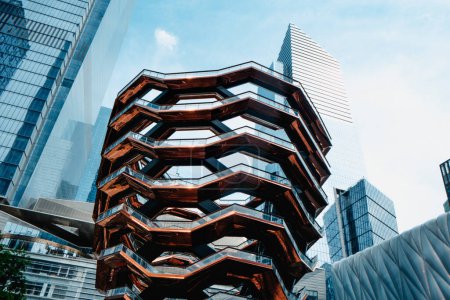 Téléchargez les photos : New York, États-Unis - 19 mai 2023 : La structure futuriste de Vessel, entourée de quelques gratte-ciel, au Hudson Yards, à New York, aux États-Unis, un jour de printemps - en image libre de droit