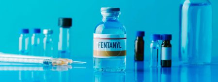 Photo for A simulated vial of fentanyl next to a syringe and some other different vials on a blue table, in a panoramic format to use as web banner - Royalty Free Image