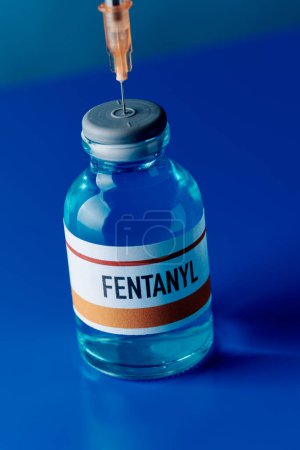 primer plano de un vial simulado de fentanilo con una jeringa pegada en su tapón sobre una mesa azul