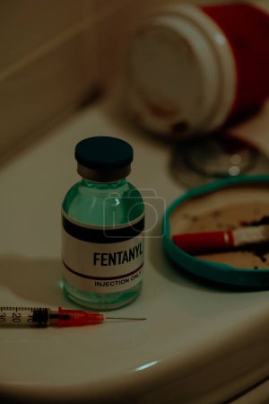 Foto de Closeup of a syringe and a simulated vial of fentanyl on the cistern of a toilet next to a cigarette butt, in a restroom - Imagen libre de derechos