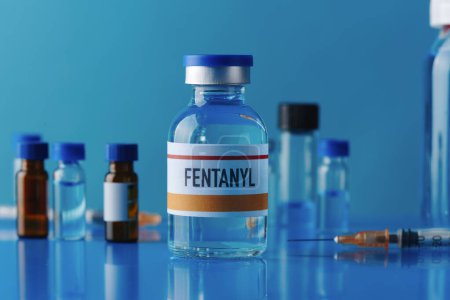 Foto de Primer plano de un vial simulado de fentanilo sobre una mesa azul junto a una jeringa y otros viales diferentes - Imagen libre de derechos