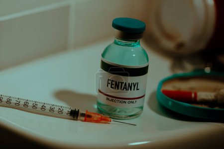 Foto de A simulated vial of fentanyl and a syringe on the cistern of a toilet in a restroom next to a cigarette butt - Imagen libre de derechos