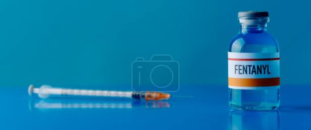 Téléchargez les photos : Une seringue et un flacon simulé de fentanyl sur une table bleue, dans un format panoramique à utiliser comme banderole ou en-tête - en image libre de droit