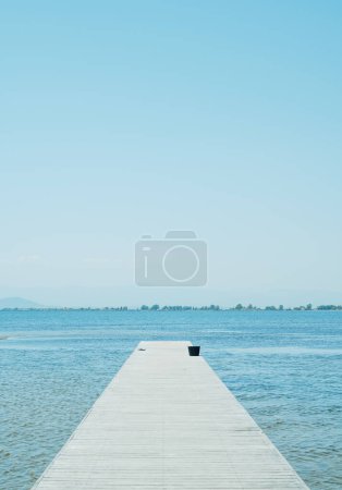 Photo for A weathered wooden pier leading to the water, with a pair of black flip-flops and a black bucket in the distance, on a summer day - Royalty Free Image