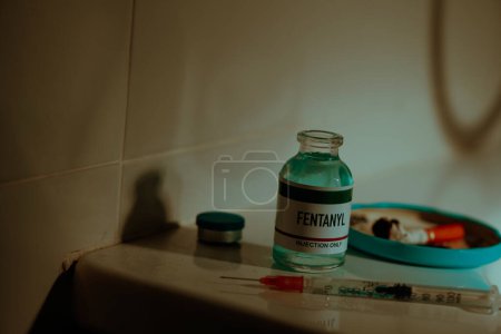 Foto de Closeup of a simulated vial of fentanyl and a syringe on the cistern of a toilet next to a cigarette butt, in a restroom, with dramatic and sordid lighting - Imagen libre de derechos