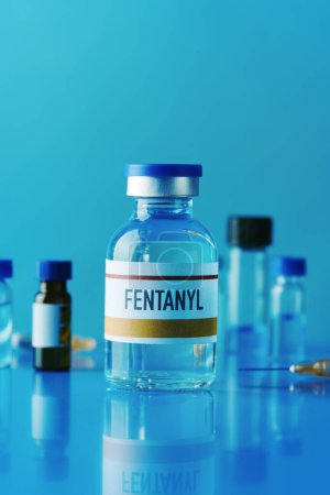 Foto de Un frasco simulado de fentanilo en una mesa azul junto a una jeringa y otros frascos diferentes - Imagen libre de derechos