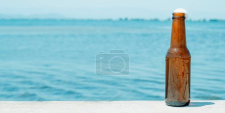 Téléchargez les photos : Une bouteille de bière rafraîchissante sur la jetée, à côté de l'eau, dans un format panoramique à utiliser comme bannière Web ou en-tête - en image libre de droit