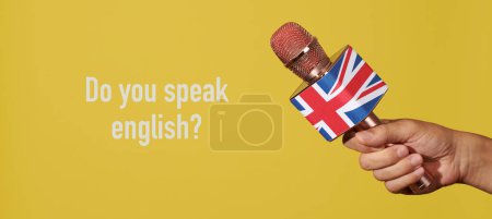 Téléchargez les photos : Un homme tient un microphone modelé avec la prise d'union, le drapeau du royaume uni, et la question parlez-vous anglais sur un fond jaune, dans un format panoramique à utiliser comme bannière web - en image libre de droit