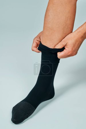 Foto de Primer plano de un hombre que se está poniendo su calcetín de compresión de pie sobre un fondo blanquecino - Imagen libre de derechos