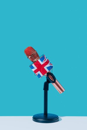 Téléchargez les photos : Gros plan d'un microphone orné du drapeau du royaume uni, dans un support noir, placé sur une surface blanche, devant un fond bleu - en image libre de droit