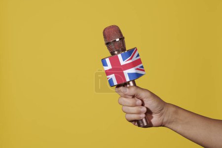 Téléchargez les photos : Un homme a un microphone avec la prise union, le drapeau du royaume uni, dans sa main, sur un fond jaune - en image libre de droit