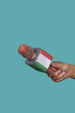 Téléchargez les photos : Gros plan d'un homme tenant un microphone orné du drapeau de l'Italie sur fond bleu - en image libre de droit