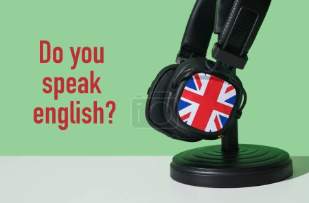 Téléchargez les photos : La question parlez-vous anglais et une paire d'écouteurs ornés du drapeau du royaume uni, sur une surface blanche, devant un fond vert - en image libre de droit
