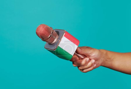 Téléchargez les photos : Un homme tient un microphone orné du drapeau italien sur fond bleu - en image libre de droit