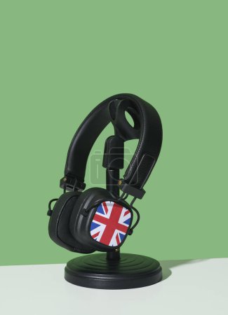 Téléchargez les photos : Gros plan d'une paire d'écouteurs noirs ornés du drapeau du royaume uni, dans un stand de bureau noir, sur une surface blanche, sur un fond vert - en image libre de droit