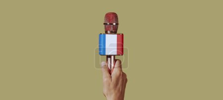 Téléchargez les photos : Gros plan de la main d'un homme tenant un microphone orné du drapeau français, sur fond brun, dans un format panoramique à utiliser comme bannière web ou en-tête - en image libre de droit