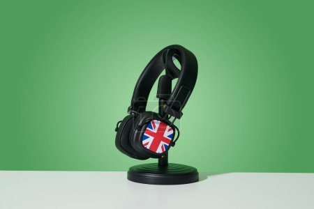Téléchargez les photos : Une paire d'écouteurs noirs ornée de la prise Union Jack, drapeau du royaume uni, placée sur un support noir, sur une surface blanche, sur un fond vert - en image libre de droit