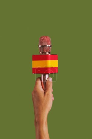 Téléchargez les photos : Un homme tient un microphone avec le drapeau de l'Espagne devant un fond vert - en image libre de droit