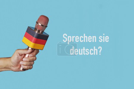 Foto de La pregunta habla alemán escrito en alemán y la mano de un hombre sosteniendo un micrófono modelado con la bandera alemana sobre un fondo azul - Imagen libre de derechos