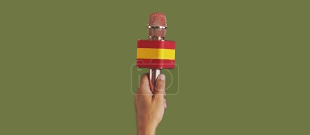 Téléchargez les photos : Homme tenant un microphone modelé avec le drapeau de l'Espagne sur un fond vert, dans un format panoramique à utiliser comme bannière web ou en-tête - en image libre de droit