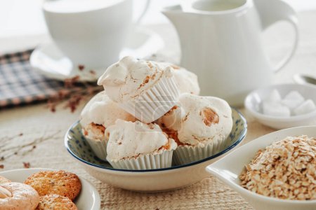 Photo for A ceramic bowl with some spanish merengues almendrados, baked meringues with almonds, on a table next to a white ceramic plate with some cookies - Royalty Free Image
