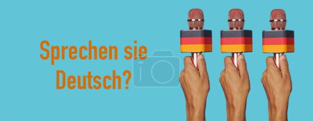 Téléchargez les photos : Mains d'homme tenant des microphones modelés avec le drapeau allemand et la question parlez-vous allemand écrit en allemand dans un format panoramique à utiliser comme bannière web - en image libre de droit