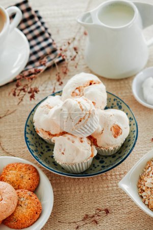 Téléchargez les photos : Quelques merengues espagnols almendrados, meringues cuites aux amandes, placés dans un bol en céramique blanche sur une table sertie d'une nappe brune - en image libre de droit