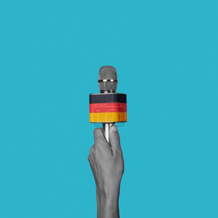 Téléchargez les photos : La main d'un homme en noir et blanc tient un microphone orné du drapeau allemand sur fond bleu - en image libre de droit