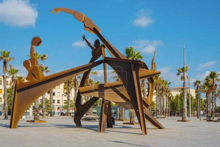 Foto de Barcelona, España - 27 de julio de 2023: Una vista de la plaza Placa del Mar en La Barceloneta, Barcelona, España, destacando la escultura Homenatge a la Natacio, homenaje a la natación como deporte, en primer plano - Imagen libre de derechos