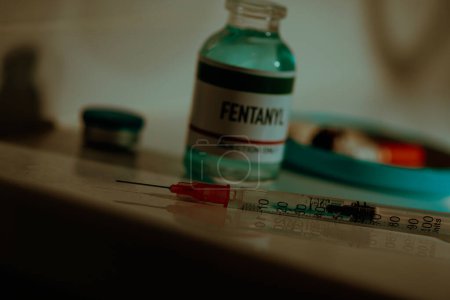 Photo for Closeup of a syringe and a simulated vial of fentanyl on a toilet cistern next to a cigarette butt, in a sordid bathroom with a dramatic lighting - Royalty Free Image