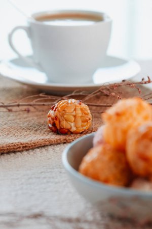 Photo for Closeup of an assortment of panellets, typical of Catalonia, Spain, eaten traditionally on All Saints Day, in a pale blue ceramic bowl on a table next to a cup of coffee - Royalty Free Image