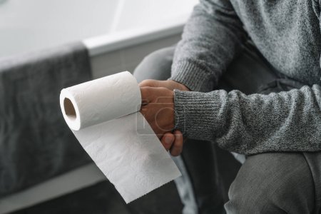 Photo for Closeup of a caucasian man, having a toilet paper roll in his hand, sitting in the toilet - Royalty Free Image